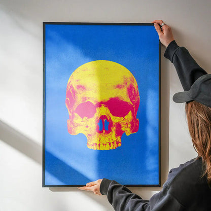 Person holding a framed Pop Art Warhol-style blue and yellow skull print on thick art paper.