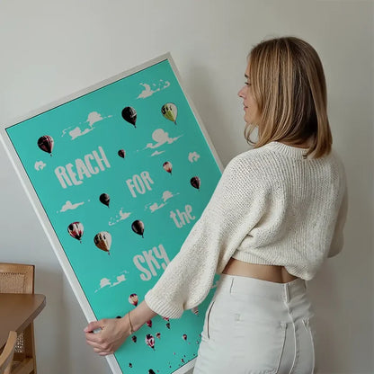 Woman holding a large "Reach For The Sky" print with colorful hot air balloons on a teal background.