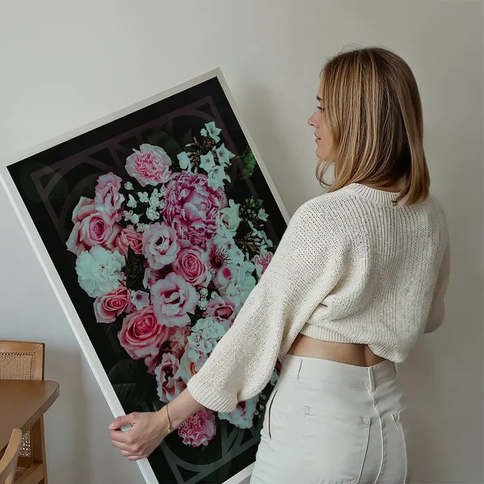 Woman holding a large framed print of pink roses with a dark geometric background.