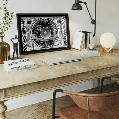 Black framed Sceno Systematis Astrology print on a light wood desk with a laptop and books.