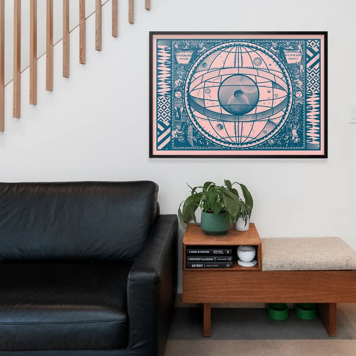Pink and teal vintage-style astrology print with an eye design, framed above a black leather sofa.