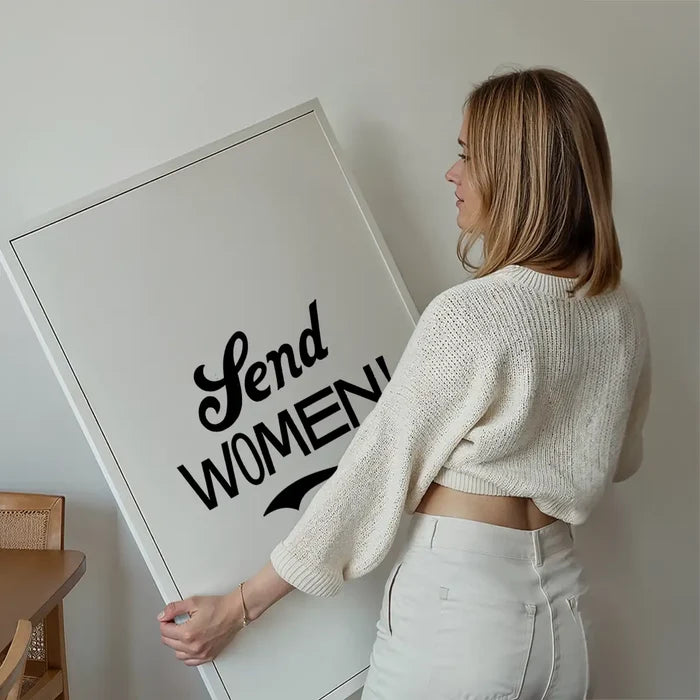 Blonde woman holding a large white framed print with "Send Women!" in bold black script.
