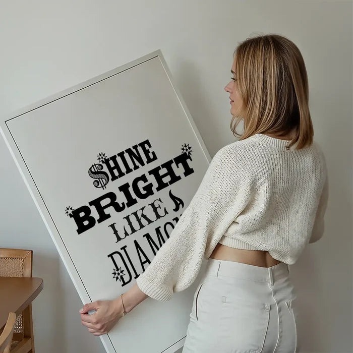 Woman holding a white framed "Shine Bright Like a Diamond" typographic print with black text.