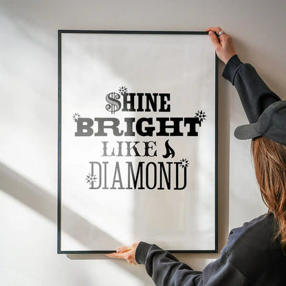 Black framed "Shine Bright Like a Diamond" typographic print on white archival paper, held by a person.