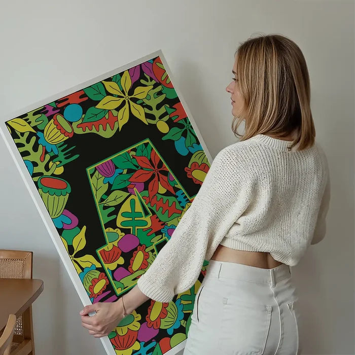 Woman holding a large green initial "A" print with colorful leafy patterns on a black background.