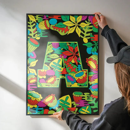 Person hanging a vibrant black poster with a green leafy "A" initial and colorful floral border.