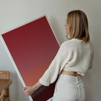 Woman holding a framed duotone Sunset 2 graphic print with red and orange hues, depicting a forest silhouette.