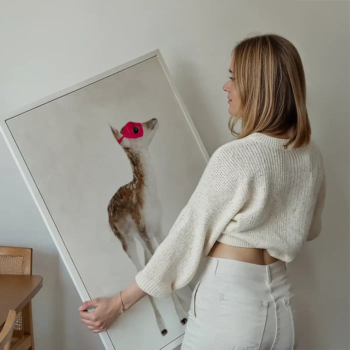 Woman holding a framed watercolor print of a fawn wearing a red superhero mask.