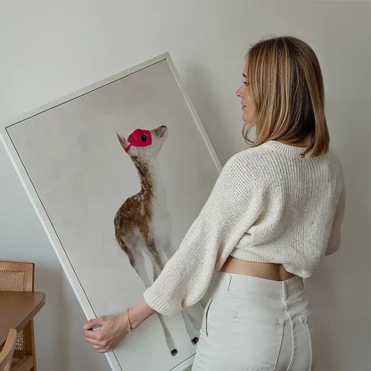 Woman holding a framed watercolor print of a fawn wearing a red superhero mask.
