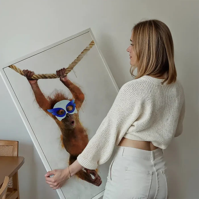 Woman holding a framed watercolor print of a super hero orangutan in a blue mask swinging on a rope.