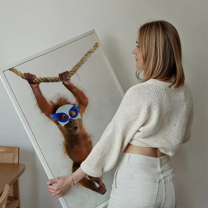 Woman holding a framed watercolor print of a super hero orangutan in a blue mask swinging on a rope.