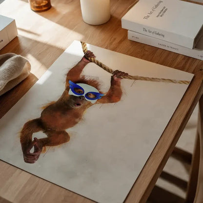 Watercolor orangutan superhero print with blue mask swinging on a rope, on a wooden table.