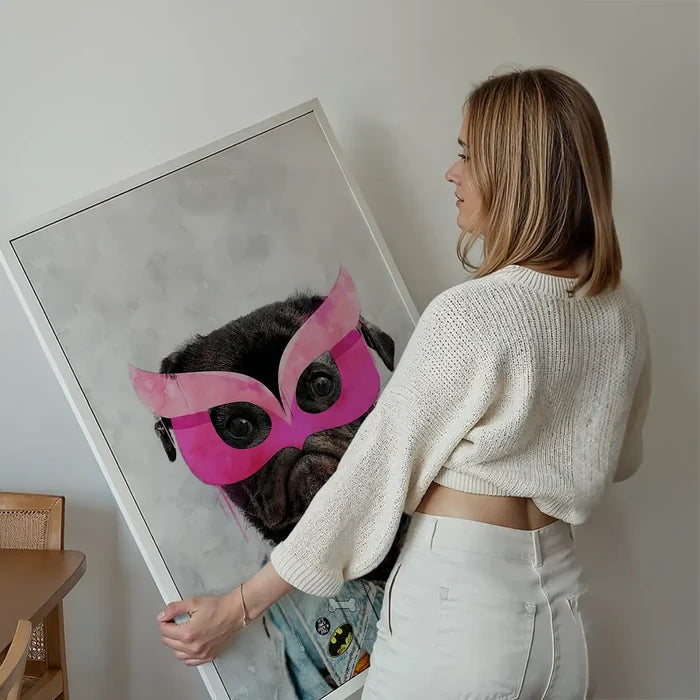 Woman holding a framed watercolor print of a black pug in a pink superhero mask and denim jacket.