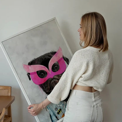 Woman holding a framed watercolor print of a black pug in a pink superhero mask and denim jacket.