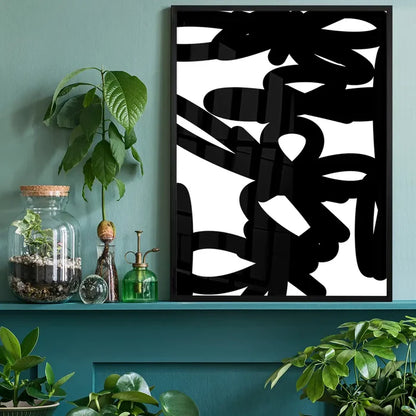 Black and white abstract graffiti-style print in a black frame, displayed on a teal shelf with plants.