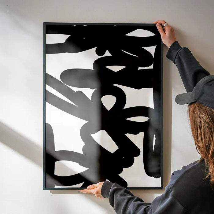 Person hanging a framed black and white tagged graffiti style print on a white wall.