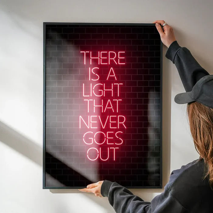 Framed art print with "THERE IS A LIGHT THAT NEVER GOES OUT" in red neon-style text on a dark brick background.