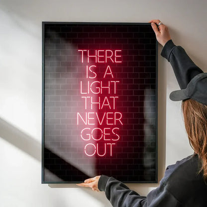 Framed art print with "THERE IS A LIGHT THAT NEVER GOES OUT" in red neon-style text on a dark brick background.
