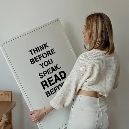 Woman holding a white framed print with "THINK BEFORE YOU SPEAK. READ BEFORE" in bold black text.
