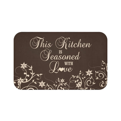 Floor mat with brown background and tan vine pattern across bottom of the mat. The phrase "This Kitchen is Seasoned with Love" is written in tan cursive script in the center.