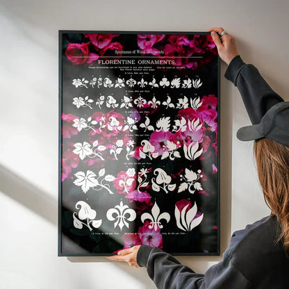 Black framed typographic floral print with white Florentine ornaments on a dark pink flower background, held by a person.