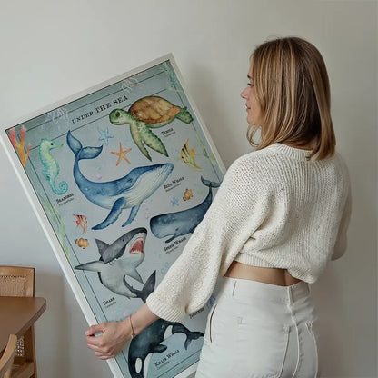 Woman holding a framed vintage-style educational print of colorful sea creatures on a light blue background.