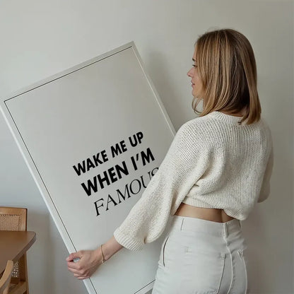 Woman holding a framed "Wake Me Up When I'm Famous" black and white typographic art print.