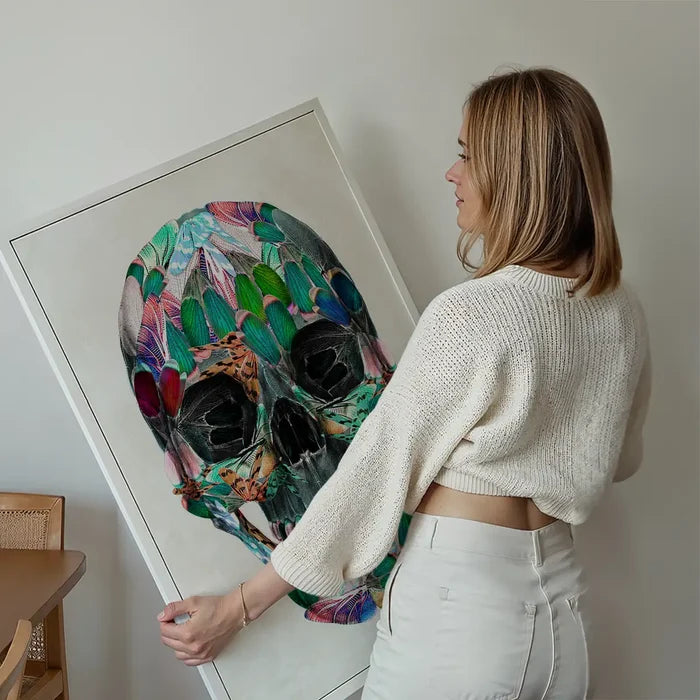 Woman holding a framed White Wings Skull Print, a colorful anatomical skull made of butterfly wings.