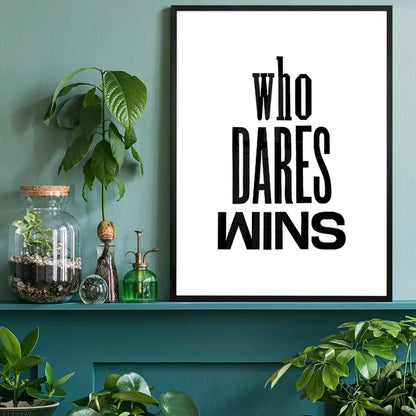 Black framed "Who Dares Wins" typographic print on white paper, displayed on a teal shelf with plants.