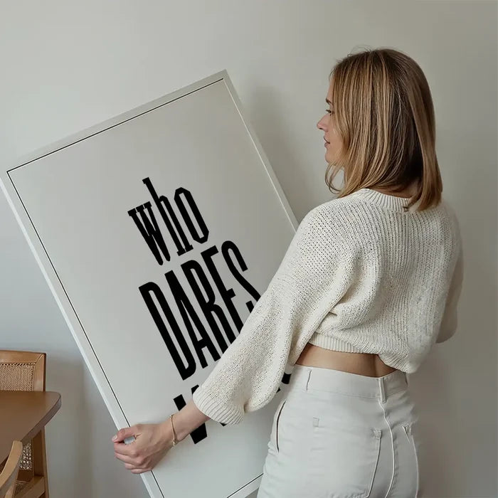 Woman holding a large white framed print with "who DARES" in bold black text, ready to hang.