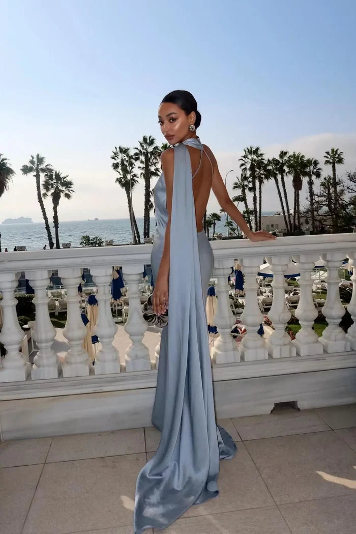 Woman in a light blue evening gown standing on a balcony with palm trees and ocean view.