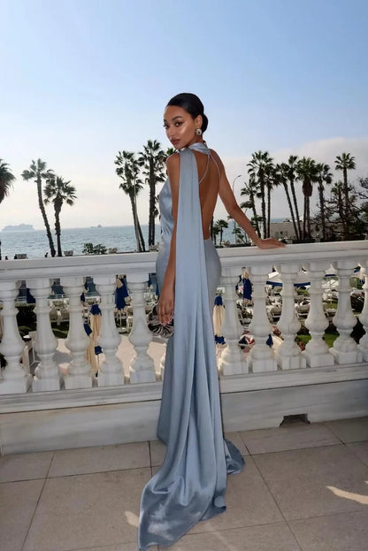 Woman in a light blue evening gown standing on a balcony with palm trees and ocean view.