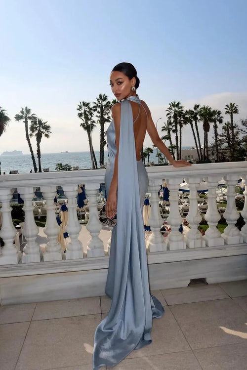 Woman in a light blue evening gown standing on a balcony with palm trees and ocean view.
